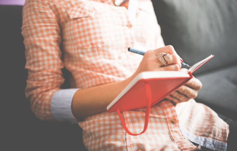 Journaling: Frau in roter Bluse schreibt in Notizbuch